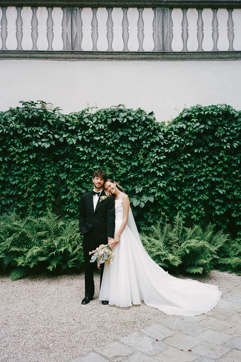 Bride and groom pose together in front of a lush ivy-covered wall at an elegant outdoor wedding venue.