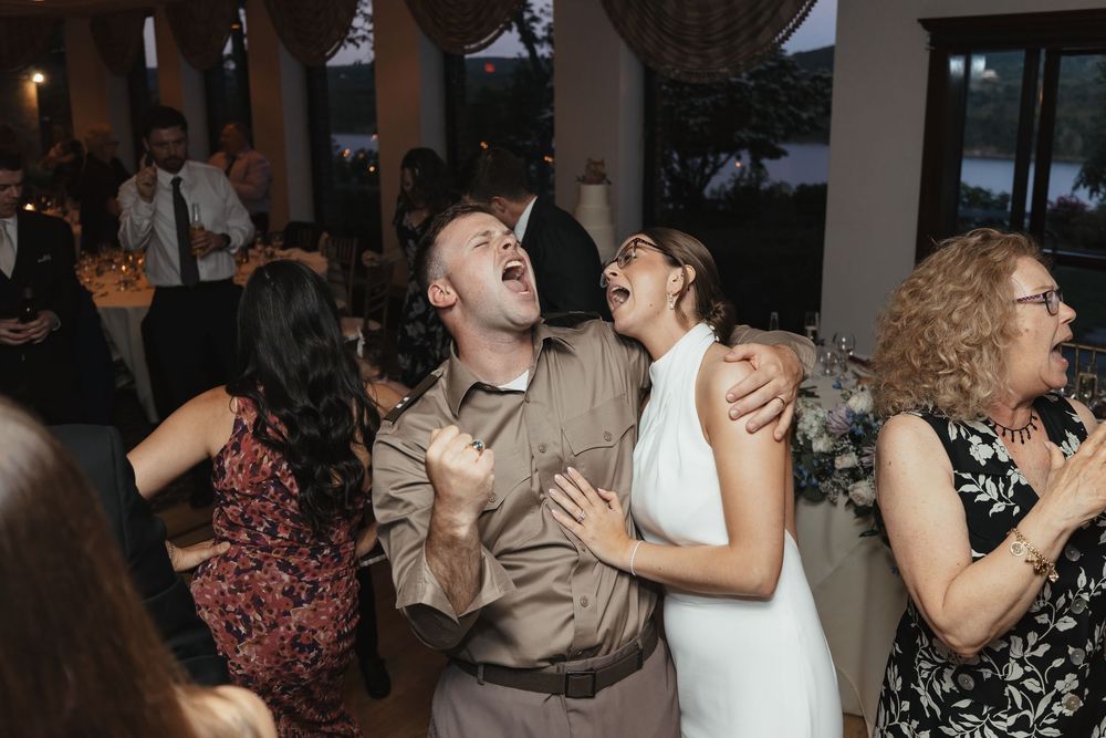 Bride in white halter gown laughs joyfully with guest while dancing at elegant wedding reception.