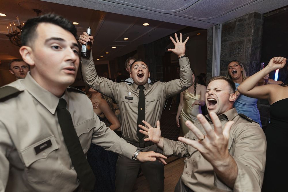 Military groomsmen in uniform celebrate energetically on the dance floor at a wedding reception.