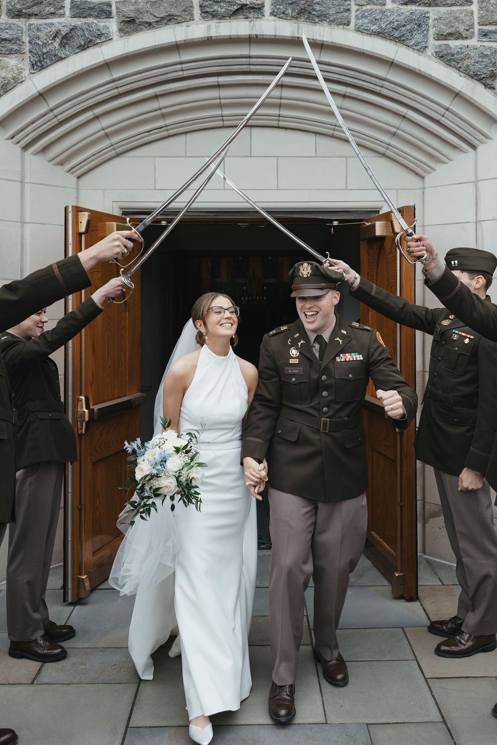 Bride and groom exit church under traditional military saber arch at West Point wedding ceremony.