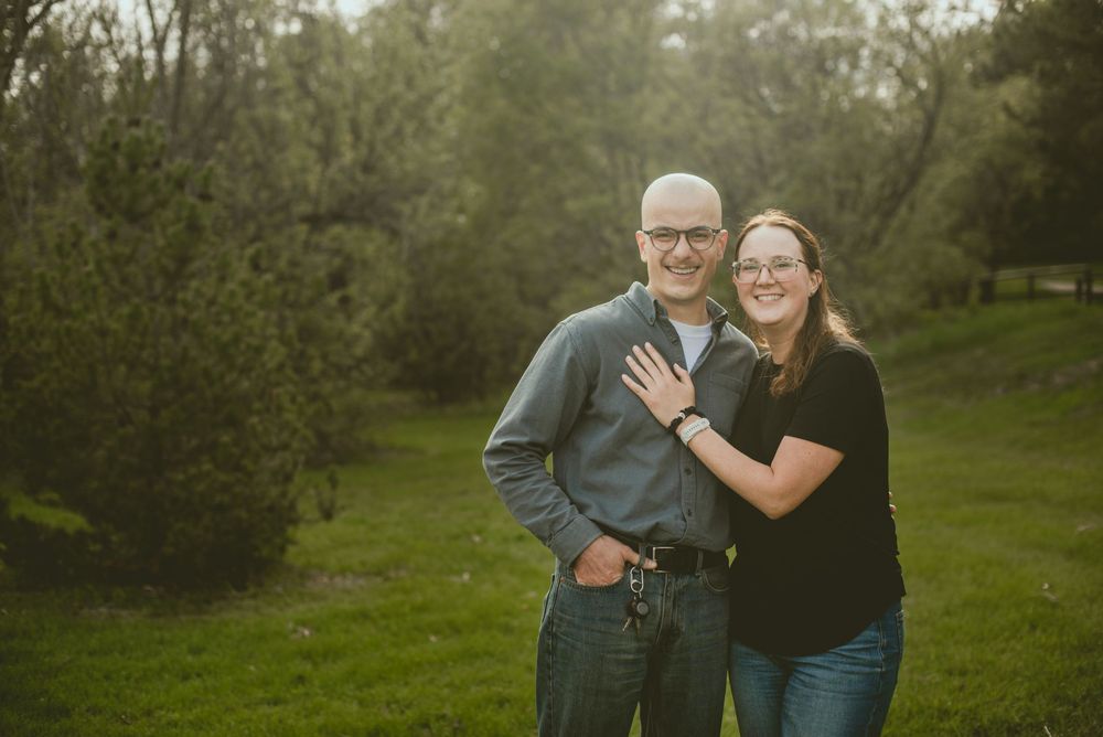 Couple smiling and embracing outdoors in a lush green park setting during golden hour.
