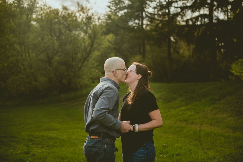 Romantic couple sharing a kiss in a sunlit green meadow surrounded by trees.