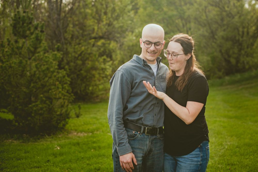 Couple smiling together outdoors in a lush green park during golden hour engagement photo session.