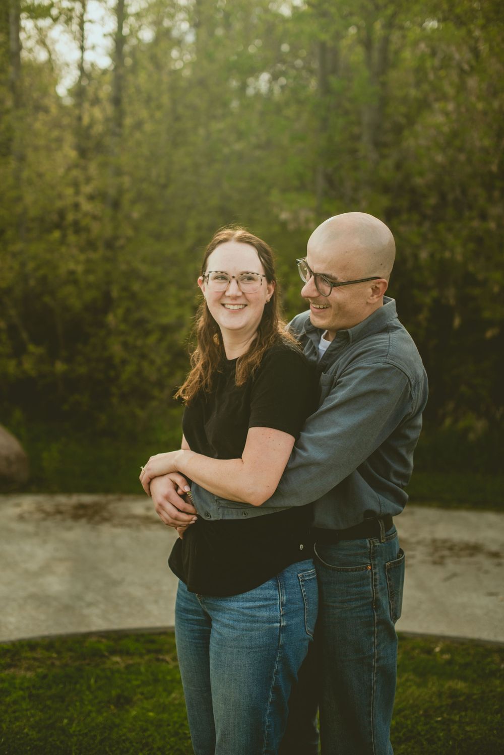 Happy couple smiling and hugging outdoors in golden sunlight after engagement proposal.