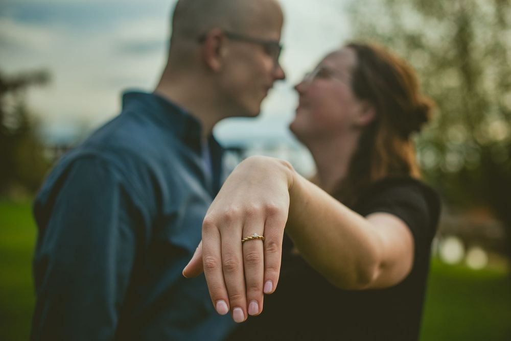 Engaged couple showing off ring while leaning in for a kiss outdoors during engagement photos.