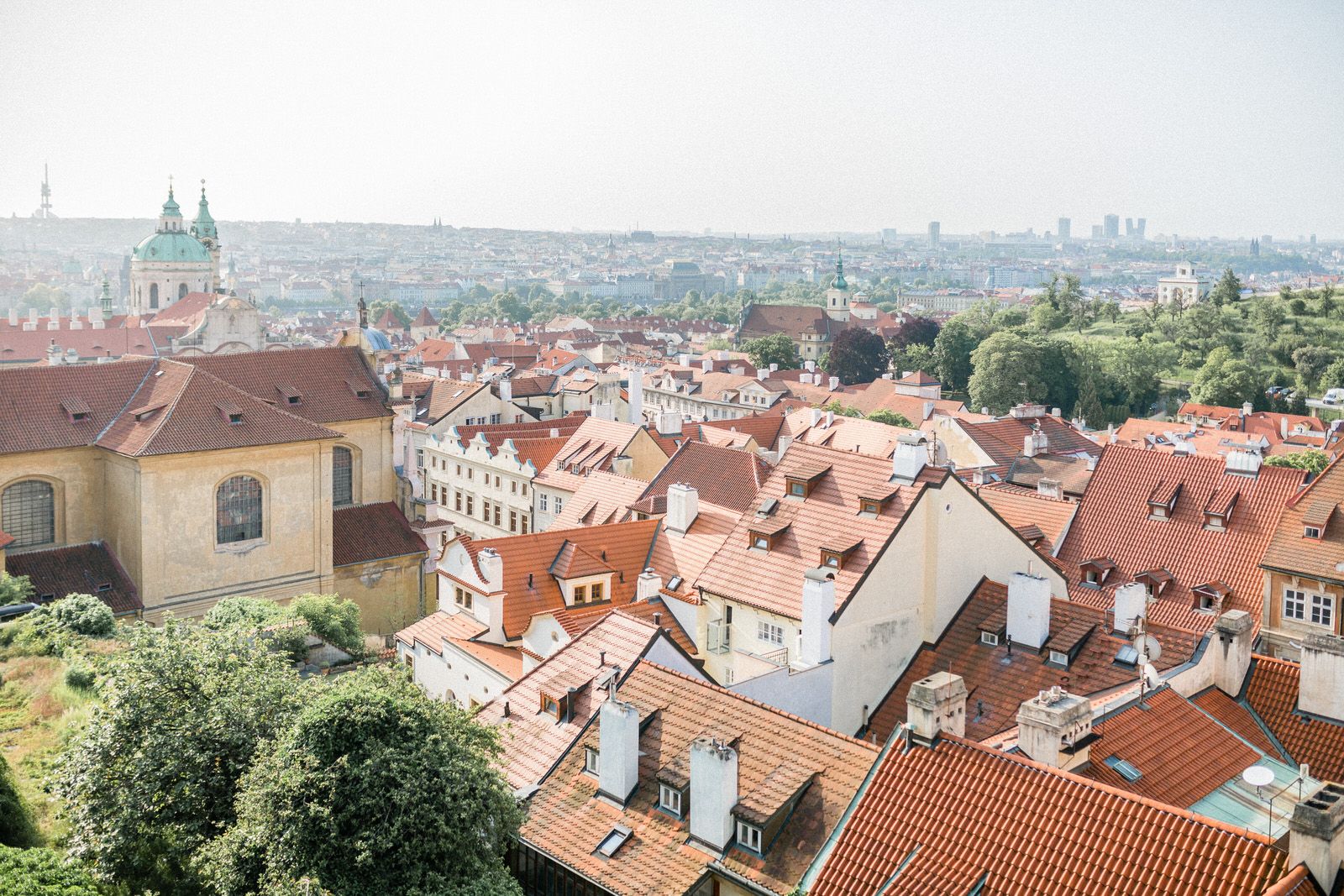 Panoramic view of Prague's terracotta rooftops and historic buildings under blue sky.