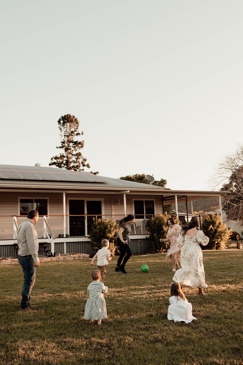 Family playing with a green ball in a backyard with solar panel rooftop home.