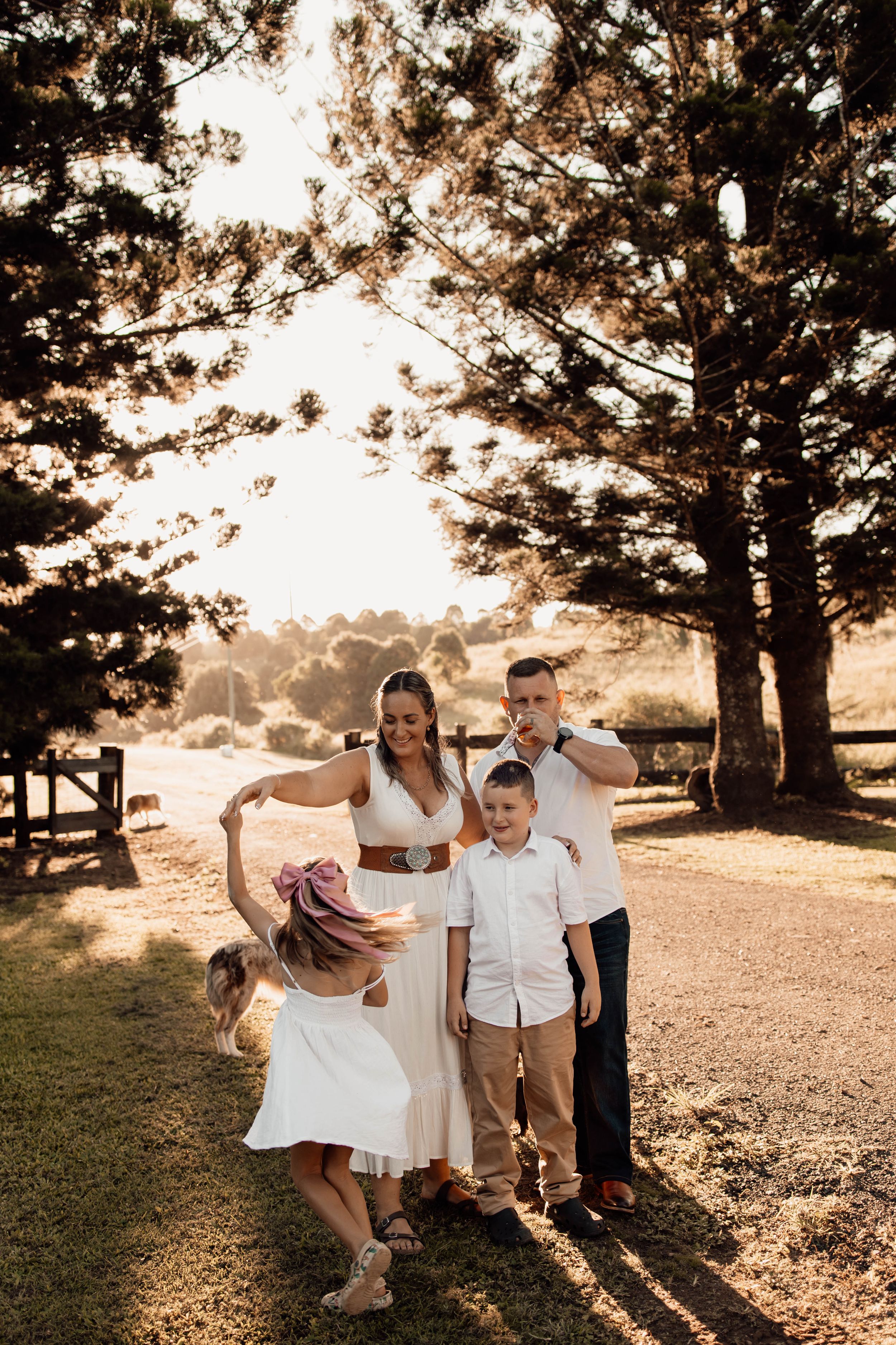 A family of four enjoys a playful moment together on a sunlit farm pathway at dusk.