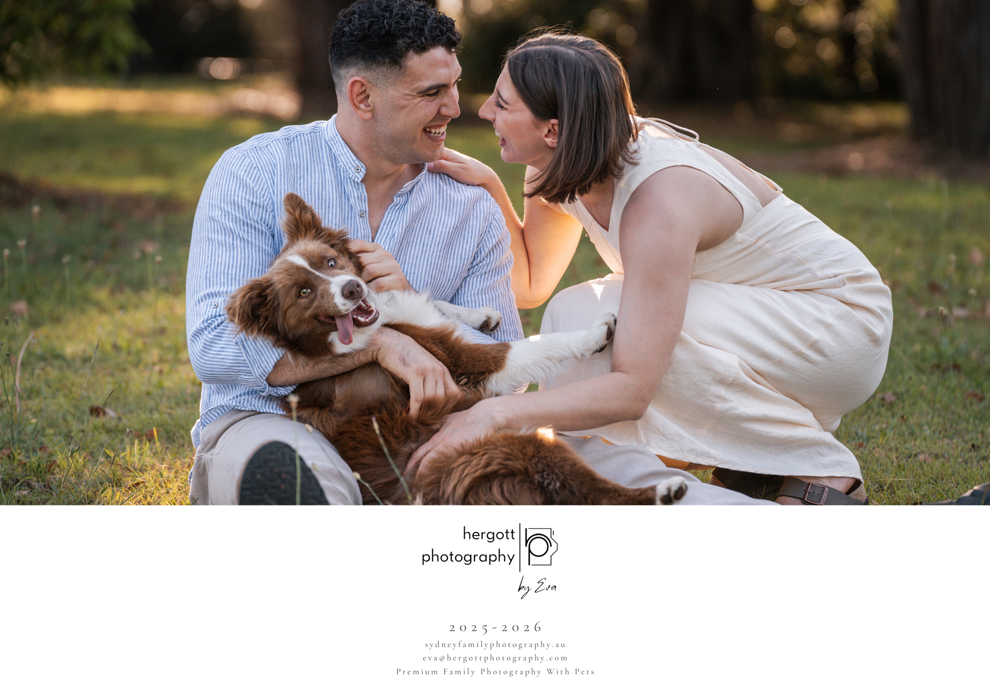 Happy couple plays with their small brown dog on grassy lawn at sunset.