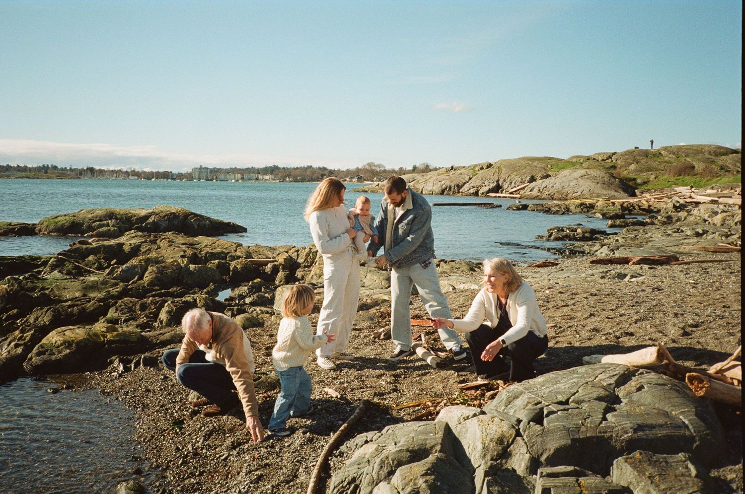 Family gathering on a rocky beach shore during a sunny day with calm blue waters in the background.