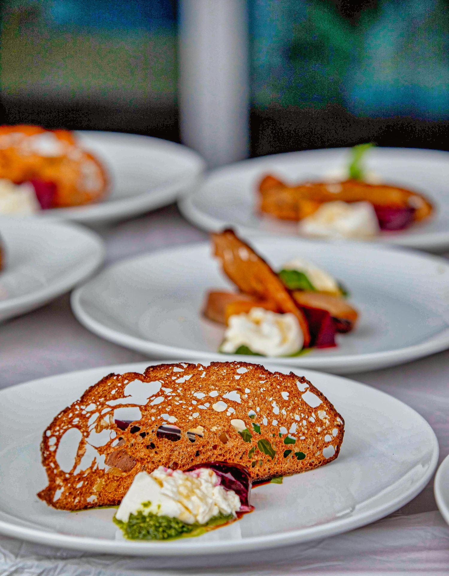 Elegant plated dessert with crispy almond tuile, whipped cream, and beet on white plates at a fine dining restaurant.