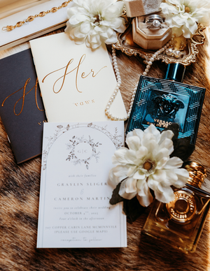 Elegant wedding flat lay with vows booklets, Versace perfume, pearl necklace, ring box, and floral invitation on fur.