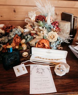 Wedding flat lay with floral bouquet, rings, pearl jewelry, perfume, and elegant invitation on wooden table.