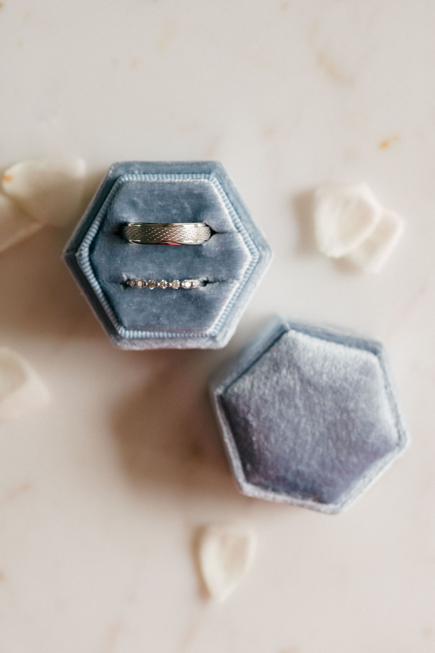 Two white gold wedding bands displayed in an open hexagonal blue velvet ring box on a marble surface.
