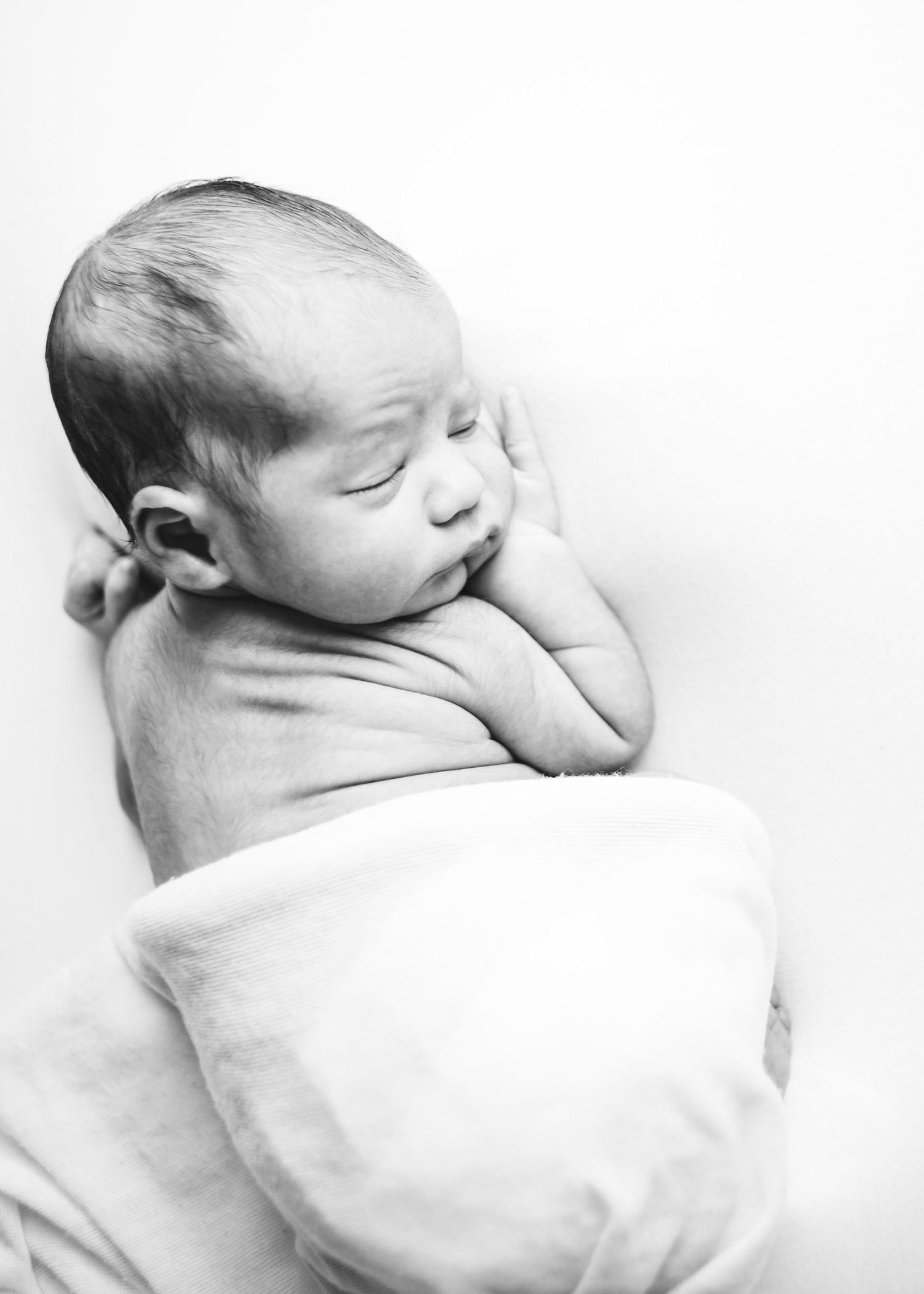Black and white portrait of a sleeping newborn baby wrapped in a white blanket