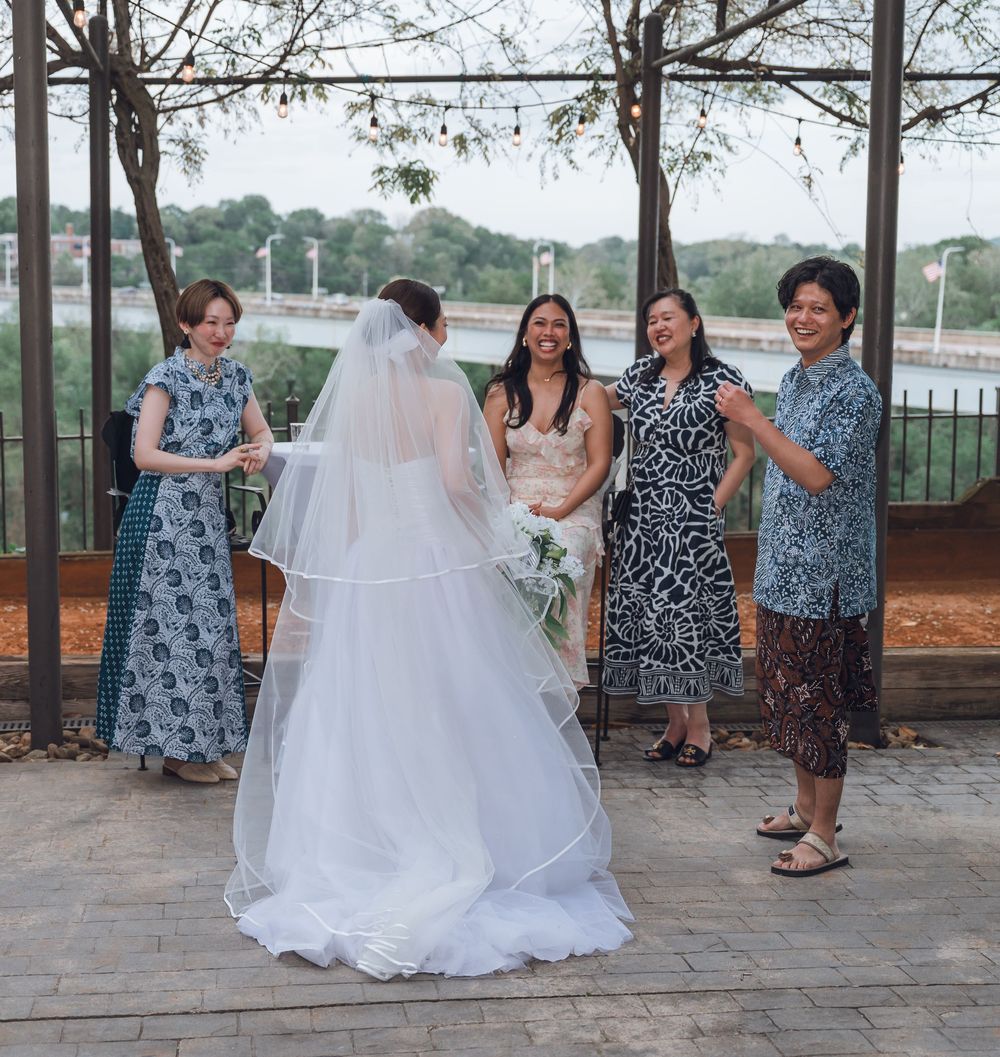 Bride in white gown and veil poses with four women in floral dresses at an outdoor wedding celebration.