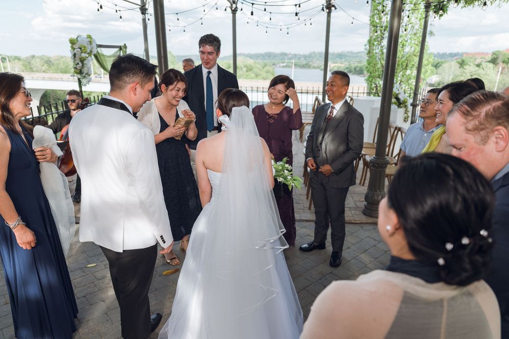 Bride and groom exchange vows surrounded by guests at an outdoor wedding ceremony with string lights overhead.