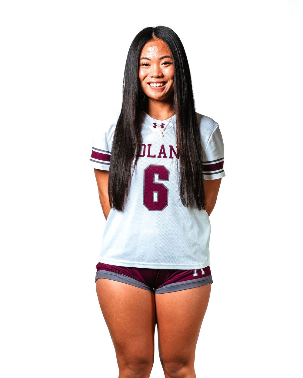 Female athlete wearing number 6 white and maroon Under Armour sports jersey and shorts smiling confidently.