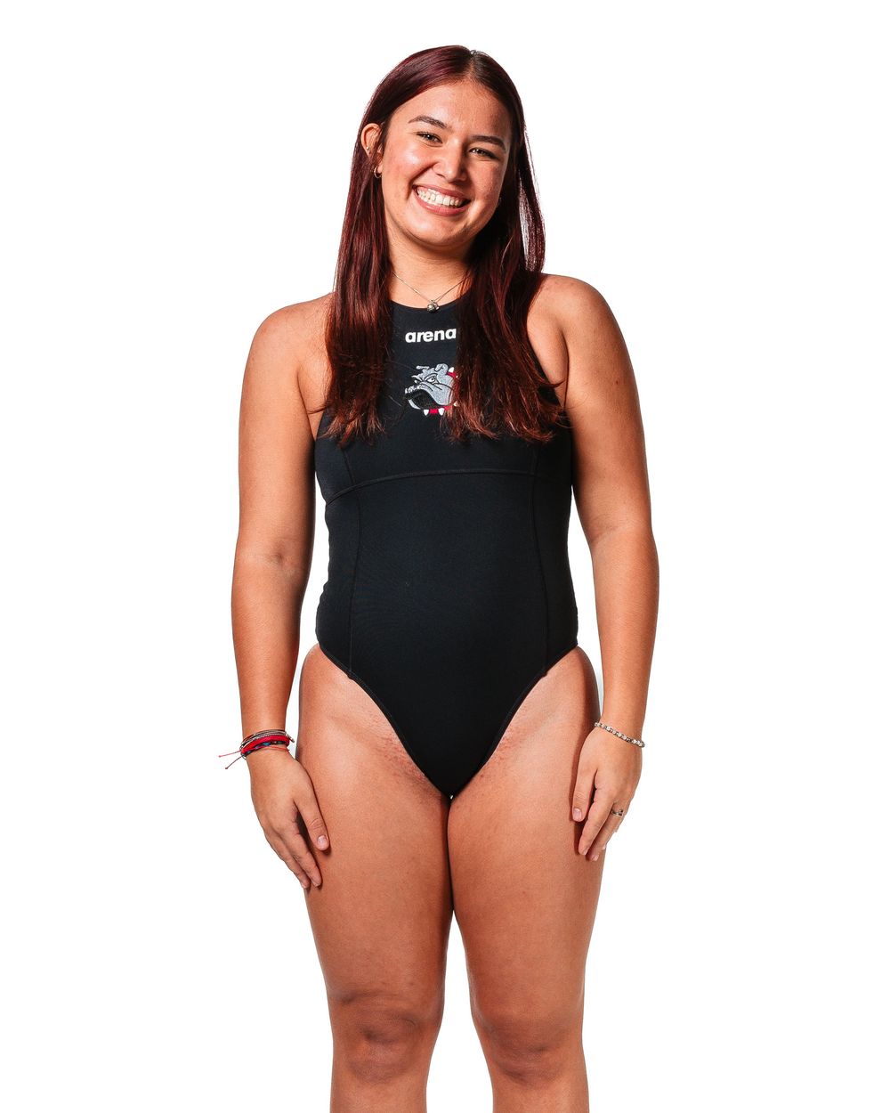 Woman smiling in black Arena one-piece swimsuit with logo detail, posing against white background.