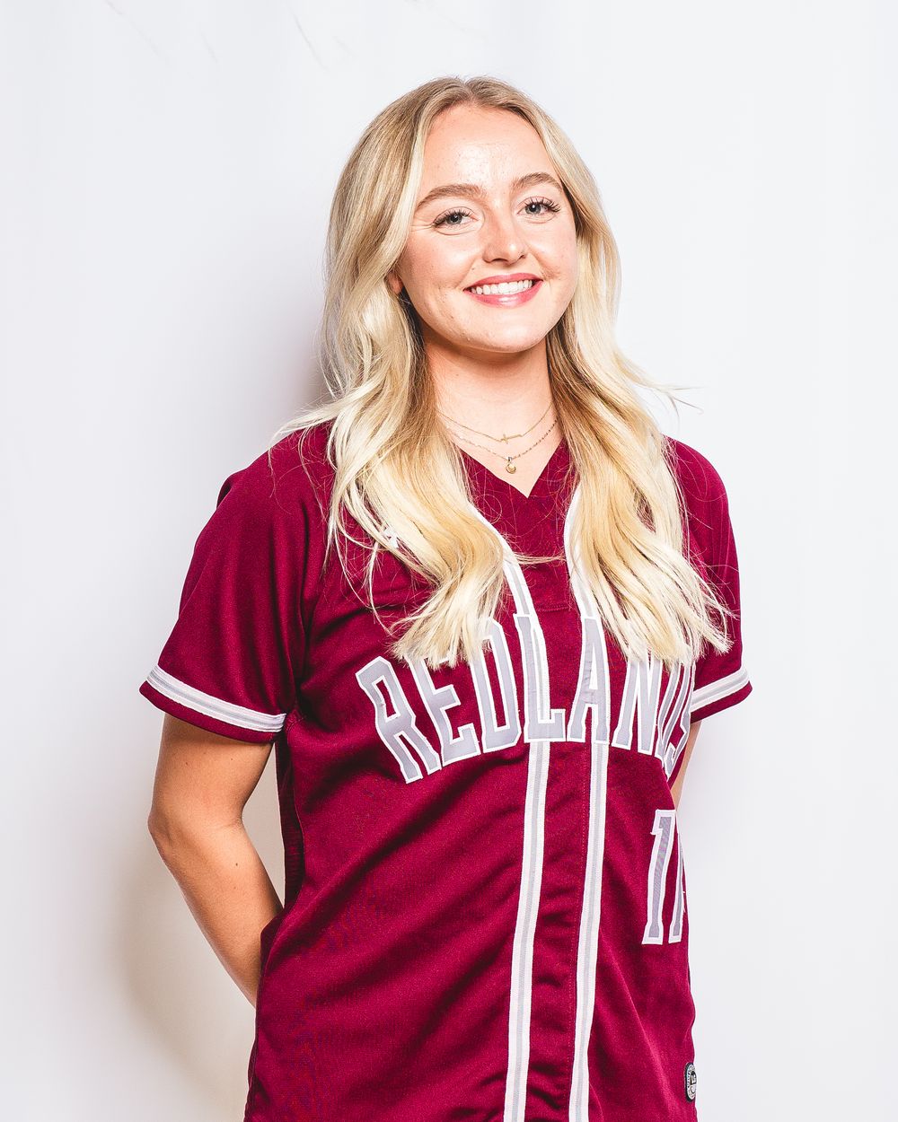 Smiling blonde woman wearing a maroon Redlands baseball jersey, posing against a white background.