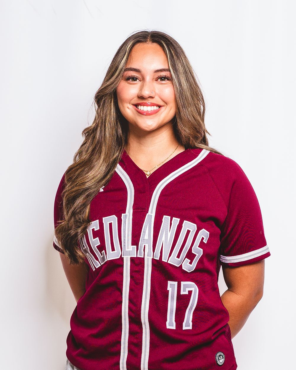 Smiling young woman wearing a maroon Redlands #17 baseball jersey poses for a sports team portrait photo.