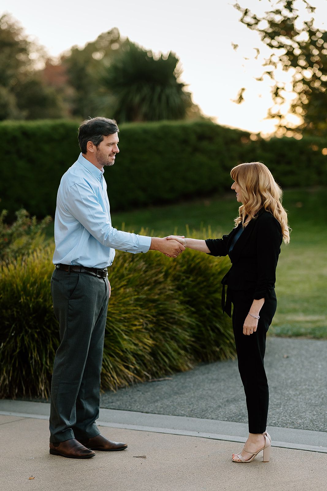 Man and woman shaking hands outdoors at sunset in a professional business greeting.