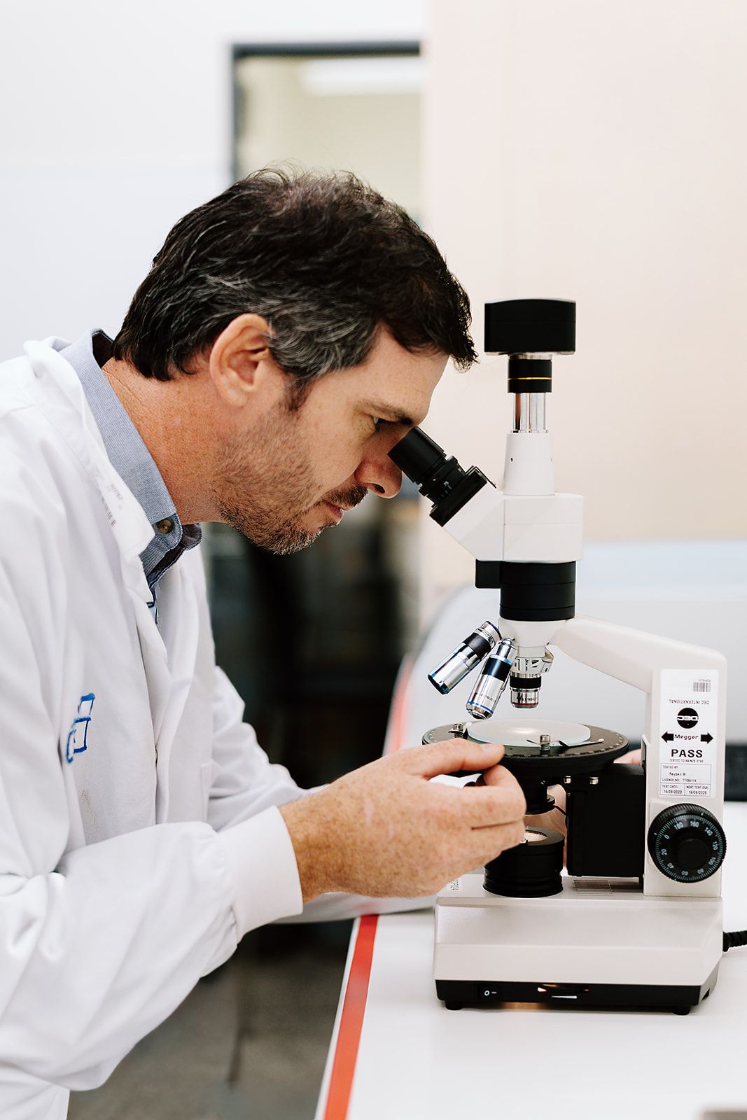 Male scientist in white lab coat examining samples through a microscope in a professional laboratory.