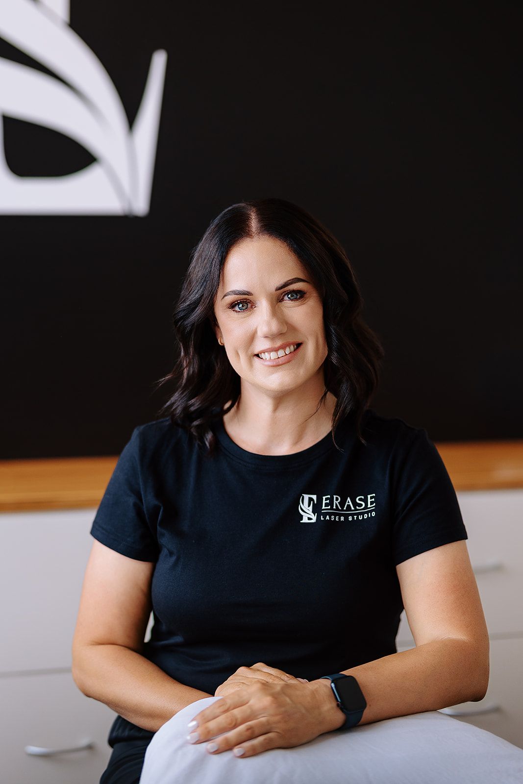 Professional woman in Erase Laser Studio black t-shirt smiling in a modern clinic setting.