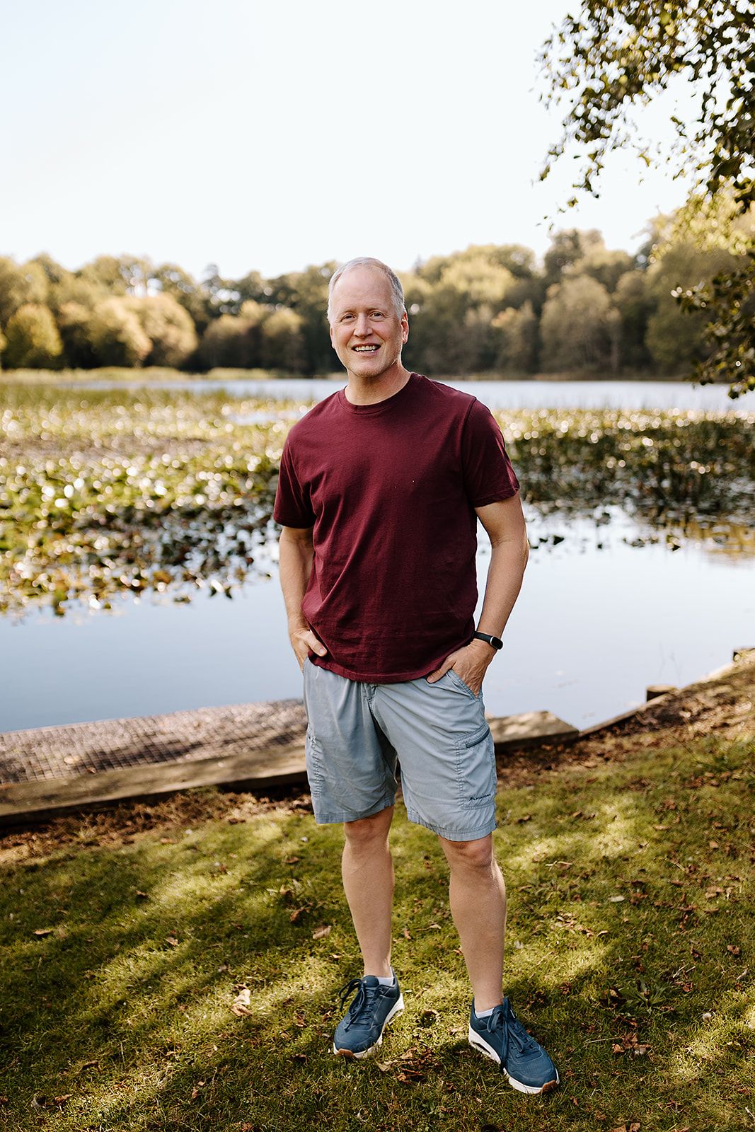Smiling middle-aged man in red t-shirt standing by scenic lake.