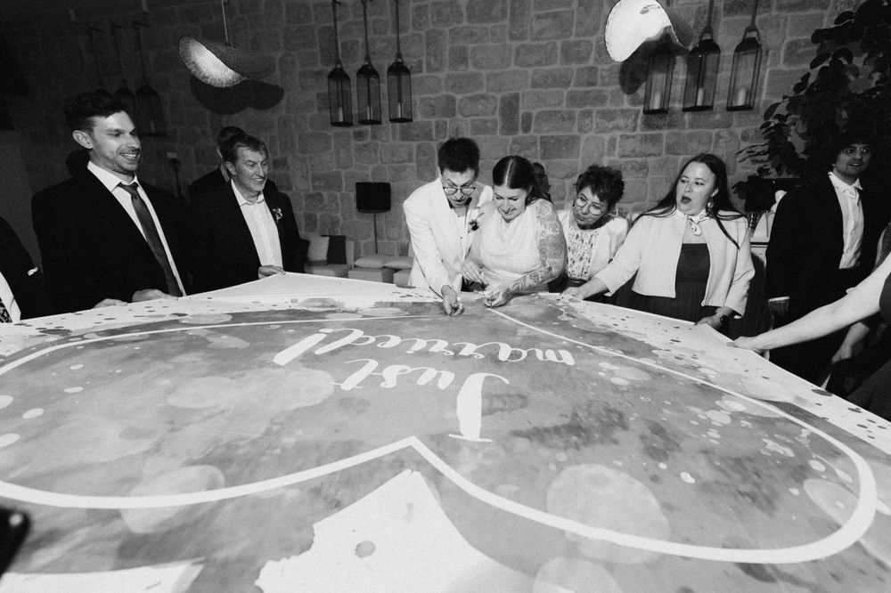 Group of people gathered around a large illuminated table with decorative script design in a black and white photo.