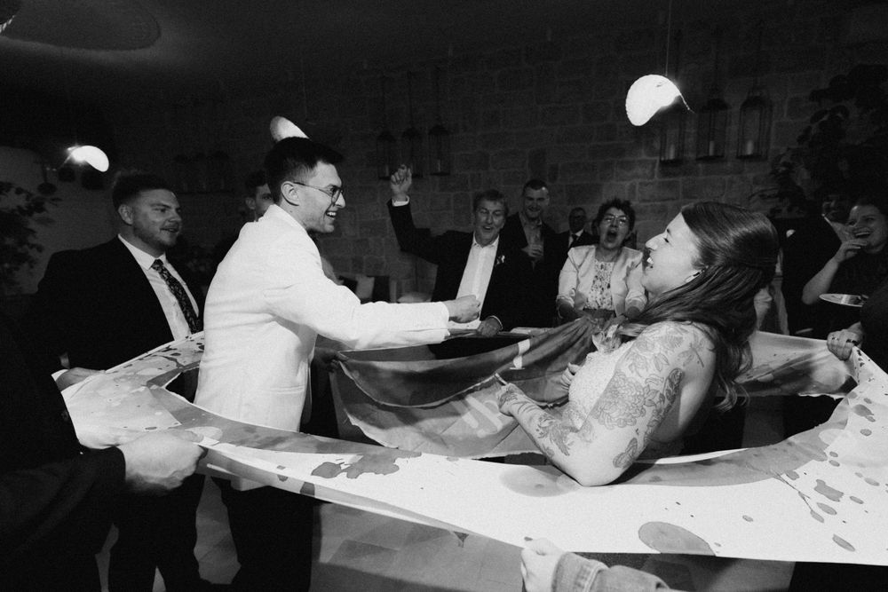 Black and white photo of guests celebrating at a lively party, with someone lying on a table surrounded by people.