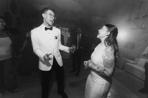 Black and white photo of a couple laughing and dancing together at a wedding reception.