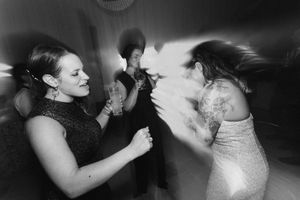 Black and white photo of women dancing energetically at a party or wedding reception with motion blur effect.