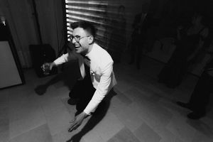 Man in glasses and white shirt dancing energetically at a party, captured in black and white photography.