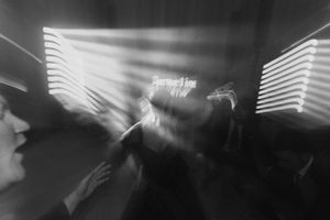 Blurry black and white photo of people dancing under bright neon lights at a nightclub.