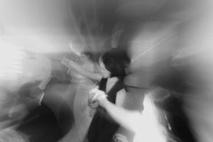 Blurry black and white photo of people dancing at a wedding reception with motion blur effect.