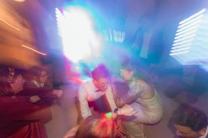 Blurred motion photo of people dancing under colorful lights at a lively party or wedding reception.