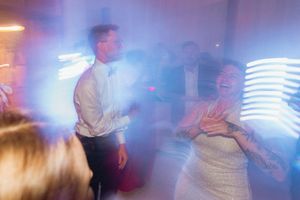 Bride and groom dancing joyfully at wedding reception with colorful neon lights and fog effects.