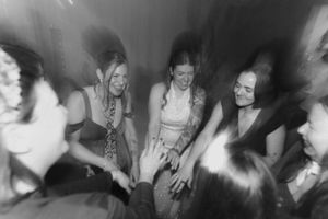 Black and white photo of smiling women gathered in a circle at a celebration, hands joined together.