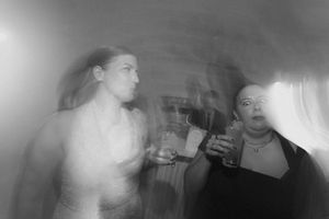 Blurry black and white photo of two women holding drinks at a party.
