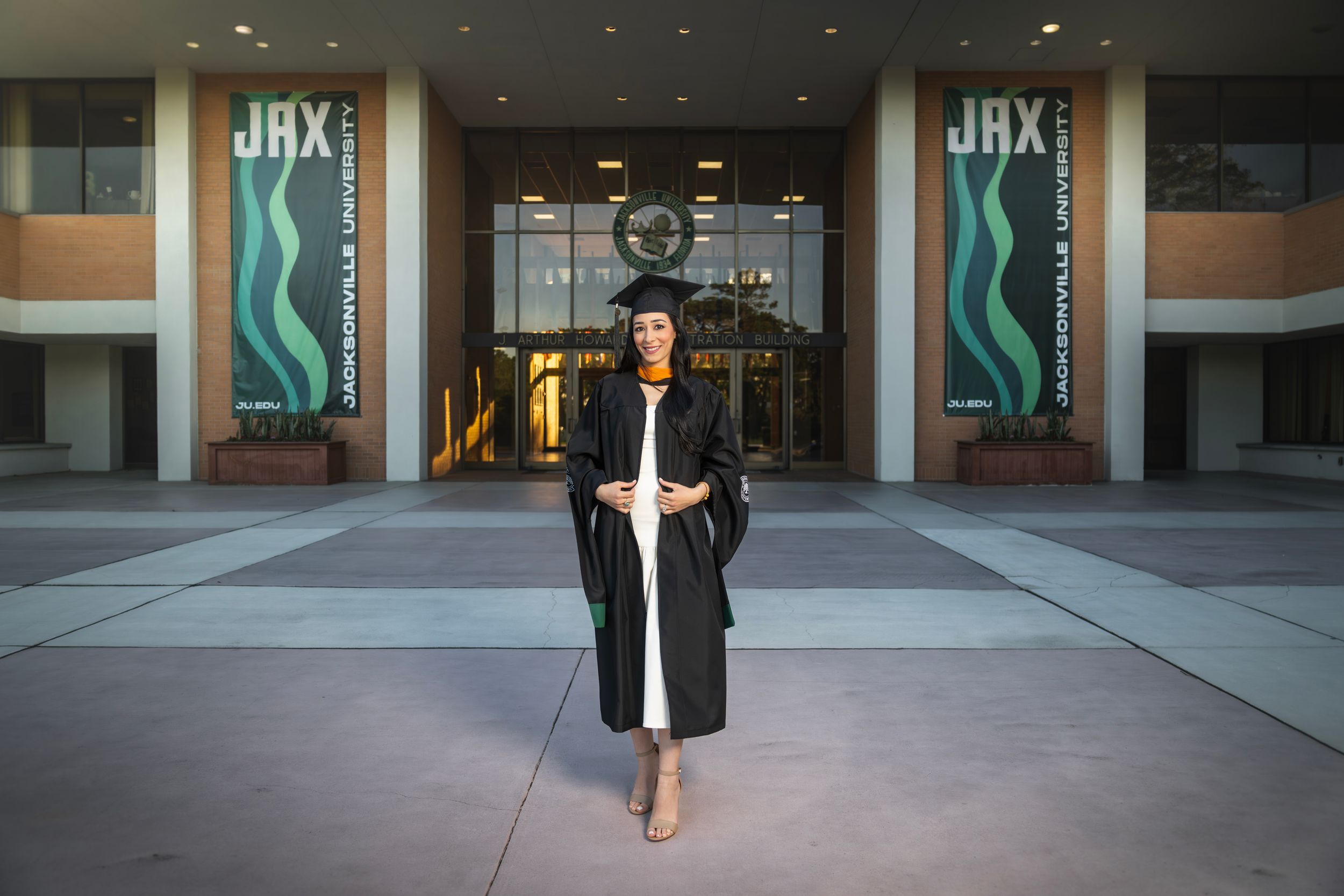 Graduate in cap and gown poses proudly outside Jacksonville University building with JAX signage.