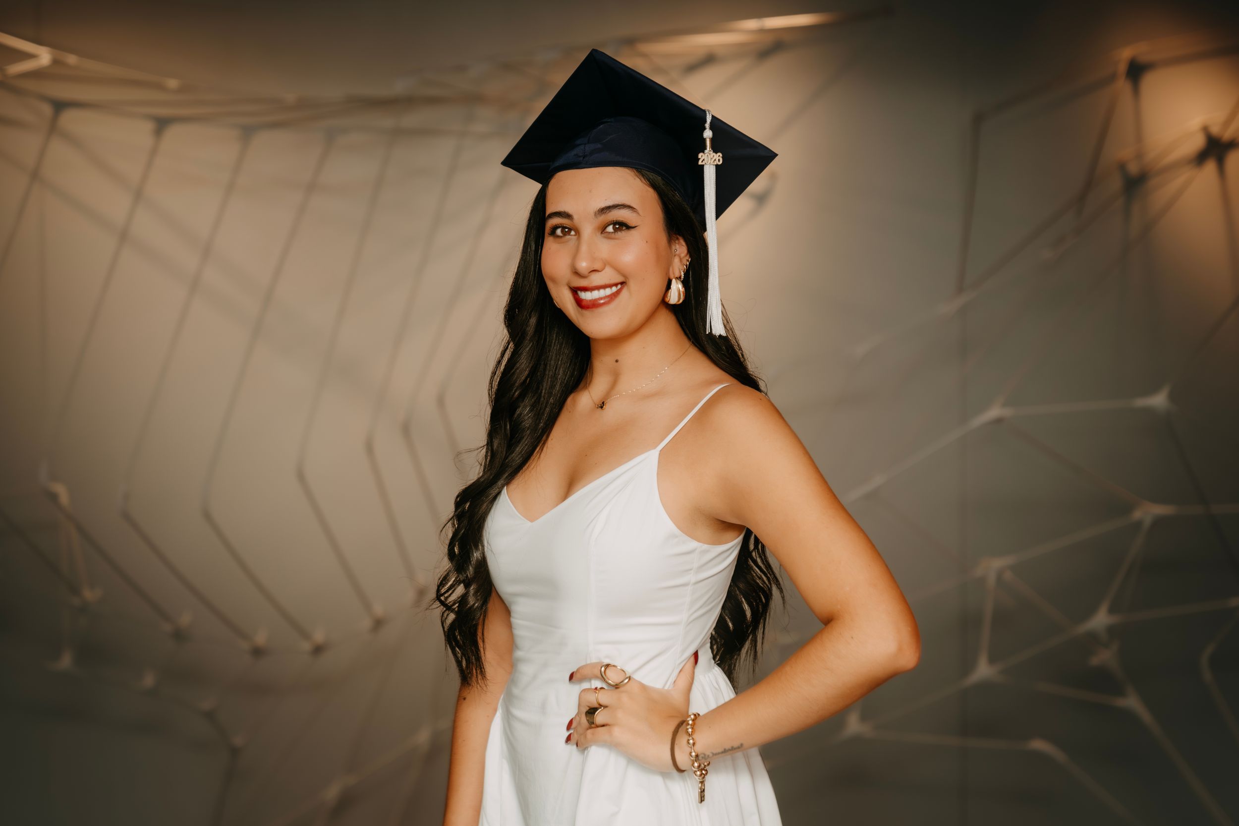 Young woman in white dress and graduation cap smiling proudly at her graduation celebration.