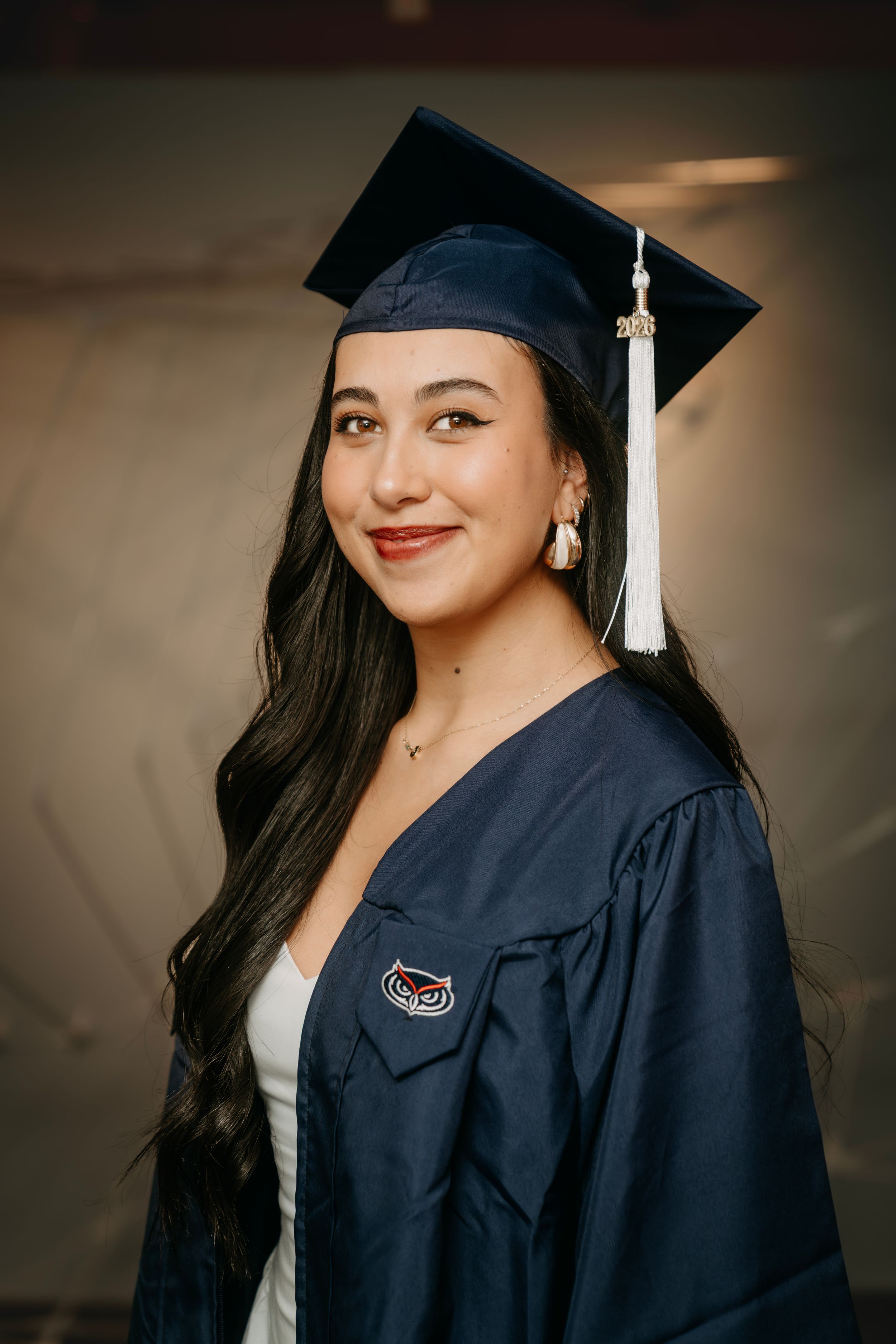 Young woman smiling in navy blue graduation cap and gown with white tassel, celebrating academic achievement.