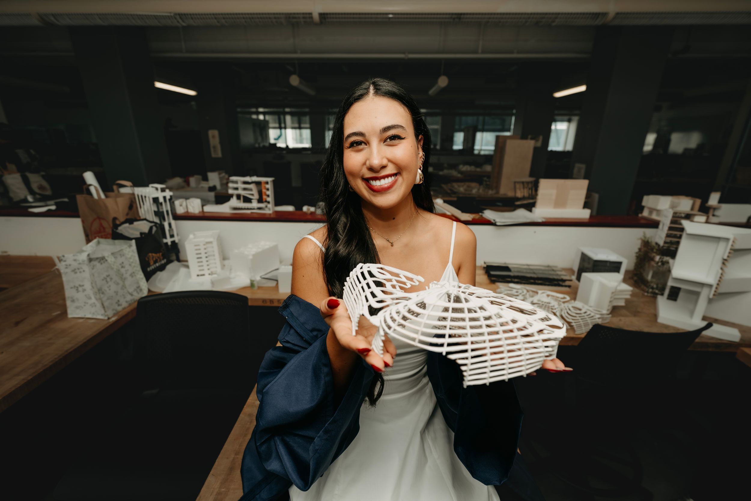Smiling woman holding a white lace corset in a wedding venue workshop setting.