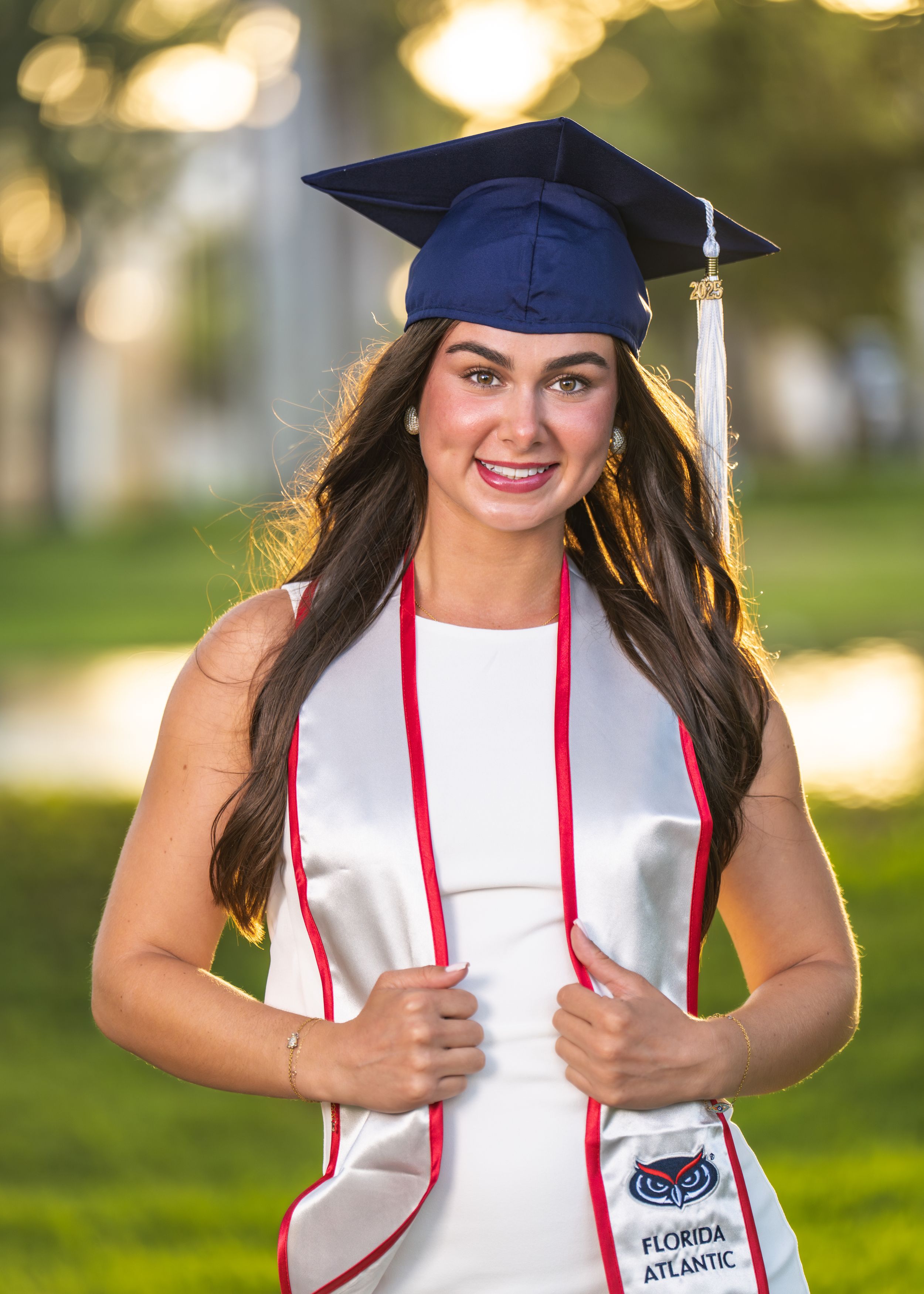 Florida Atlantic University graduate smiling in navy cap and white graduation stole outdoors.