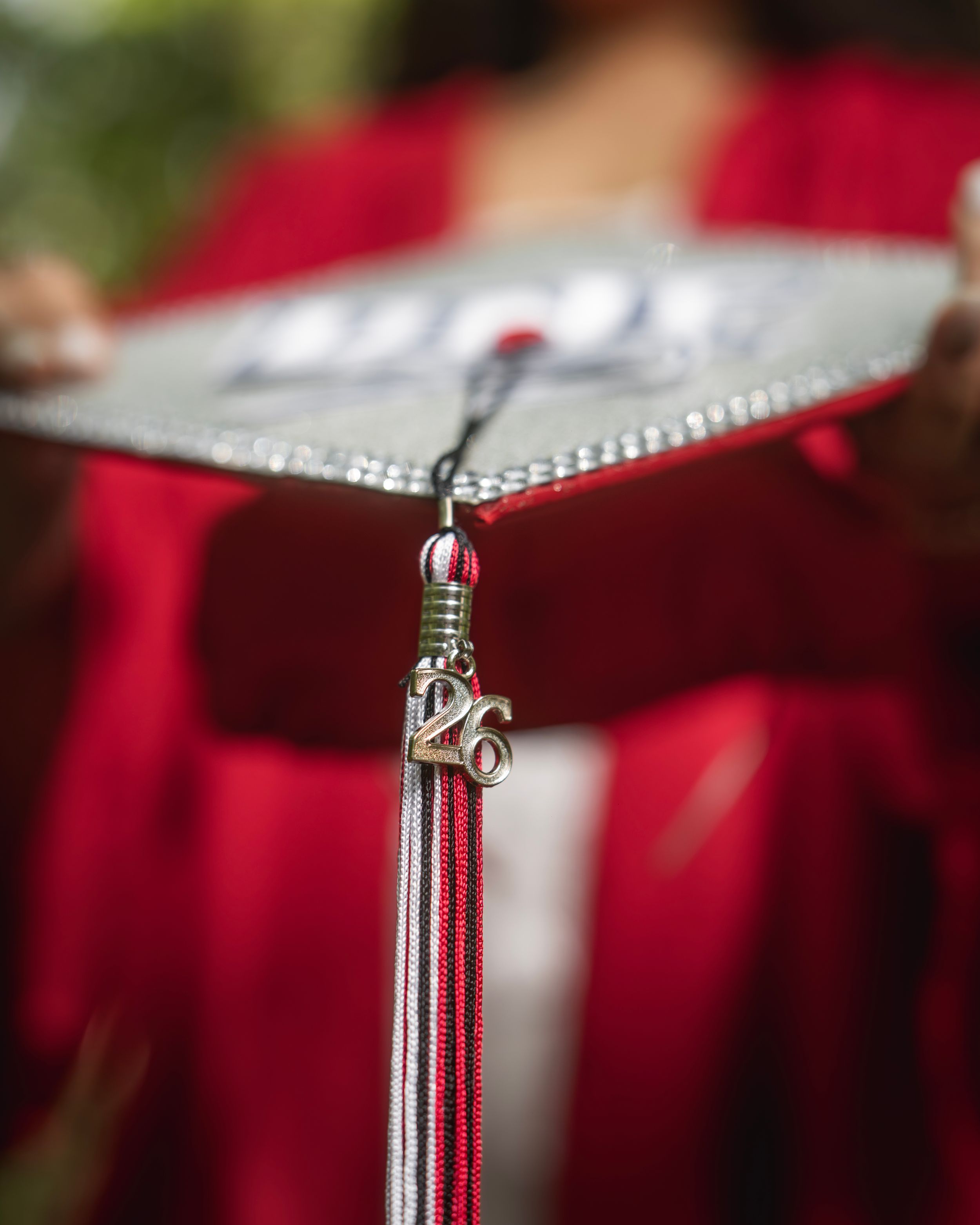 Close-up of a UNF graduation cap tassel with a 26 charm in red and silver colors.