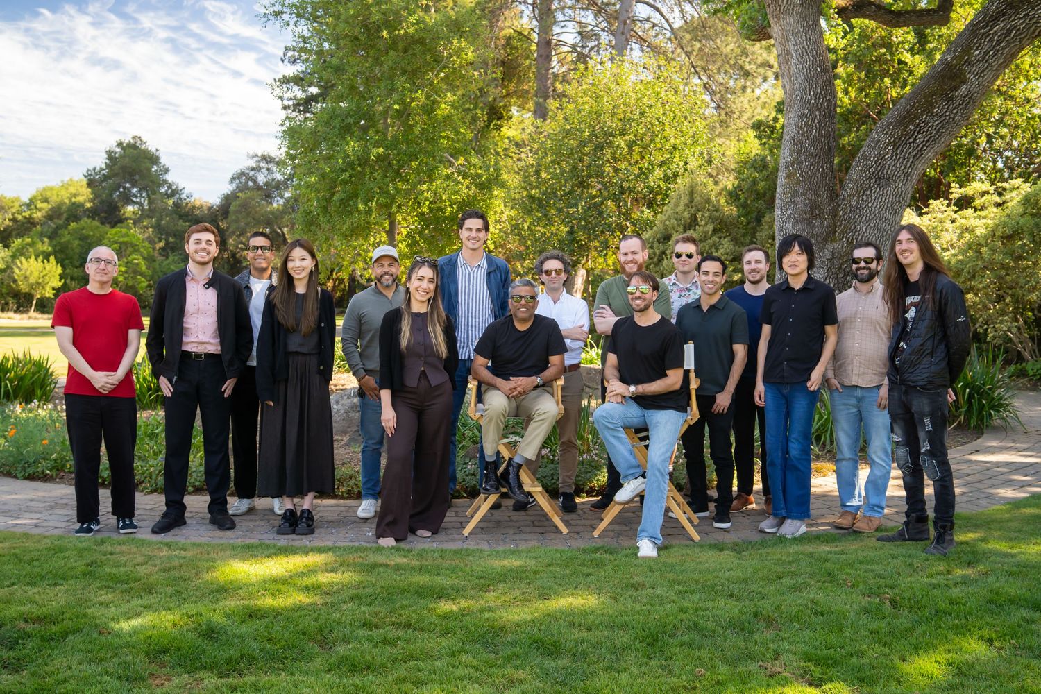 A diverse group of professionals posing together outdoors in a lush garden setting on a sunny day.