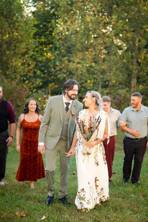 Bride and groom walking with guests in a green outdoor autumn wedding setting.
