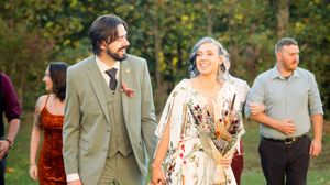Smiling bride and groom holding hands while walking outdoors at a fall wedding.