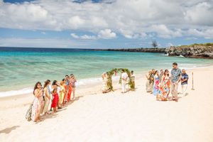 Guests gather for a tropical beach wedding ceremony in Hawaii with turquoise ocean waters in the background.